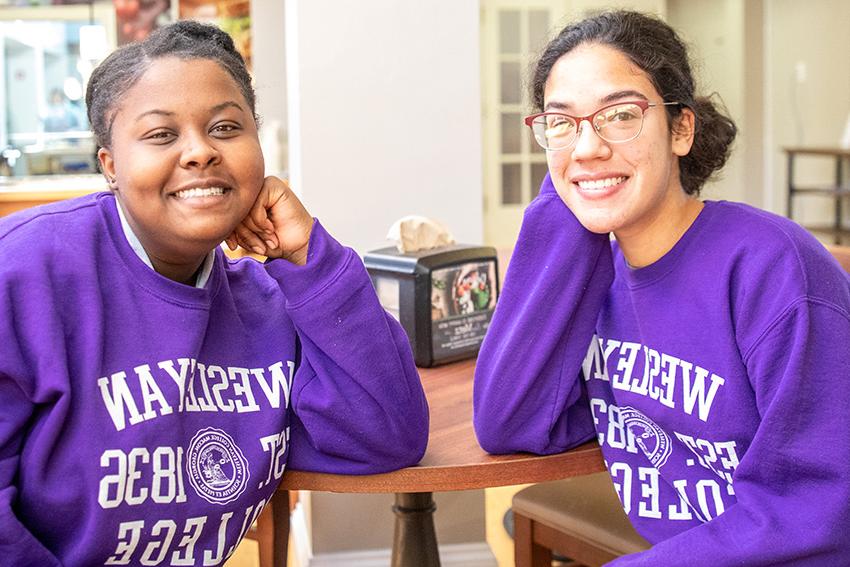two students sitting at table with purple sweatshirts on