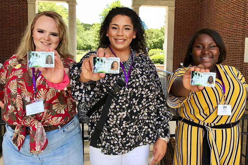 Three students hold up their new student id badges